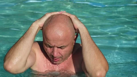 Bald middle aged man washes his face in swimming pool on summer day Stock Footage 308219810