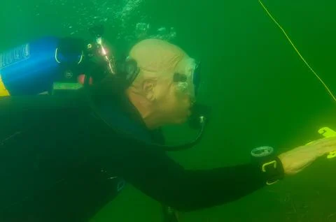 A bald SCUBA diver exploring a murky inland lake with dive flag line in hand Stock Photos