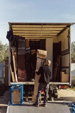 Bald worker holds bundle while co-worker tries to lift it onto moving truck Stock Photos