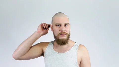 Bald young man with a beard combing his bald head with a comb and cries Stock Footage 122012388