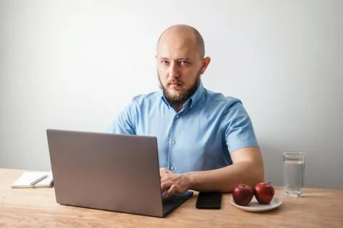 Bald young man with beard working online on his laptop at the wooden table Stock Photos