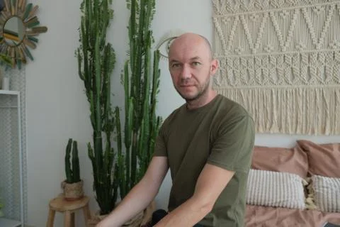 A bald young man sitting on the bed. The guy in the green shirt Stock Photos