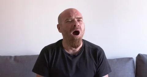 Bald young man yawning while sitting on the couch Stock Footage 303503264