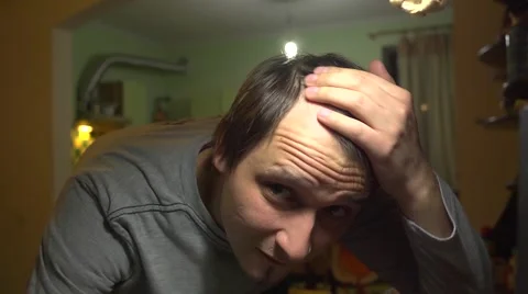 Balding young man looking at himself in the mirror with disappointment Stock Footage
