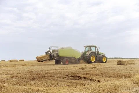 Bale of Hay Being Collected While a Tractor Operates in a Field, Under a Sky Stock Photos