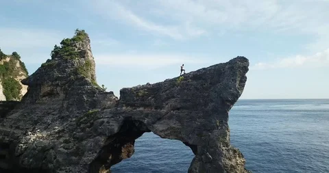 Bali Man Walking on Mountain Top Stone Arch Drone Shot Stock Footage 106786806