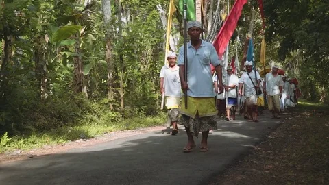 Balinese procession going to temple through forest road with flags, editorial Stock Footage 77895630