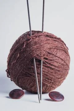 A ball of brown thread and two knitting needles in it. Nearby are two brown butt Stock Photos