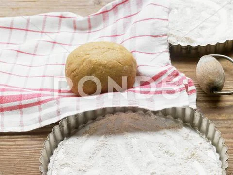 A ball of dough on a tea towel next to a floured quiche dish Stock Photos