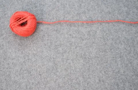 A ball of red yarn with a loose string stretching to the side on a gray backg Stock Photos