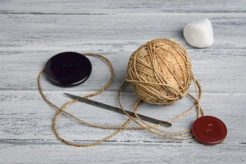Ball of thread, buttons, long needle on a wooden background Stock Photos