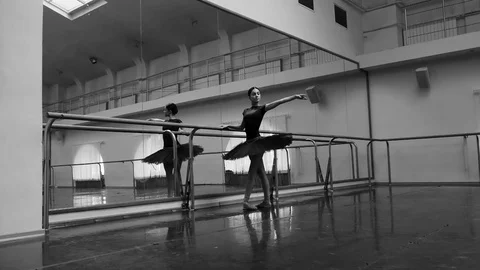 Ballerina in black tutu and pointe stretches on barre in ballet gym. Woman Stock Footage