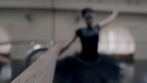 Ballerina in black tutu stretches on barre in ballet gym. Woman standing near Stock Footage