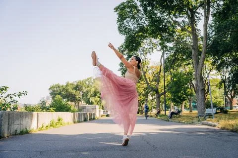 Ballerina dancing en pointe elevating leg in urban park Stock Photos