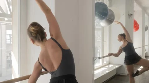 A ballerina performs movements while standing at the barre in front of a mirror. Video stock 287238807