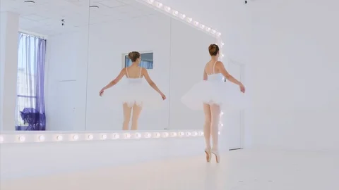 Ballerina in white tutu is practicing dance elements in front of the mirror. Video stock 111752648