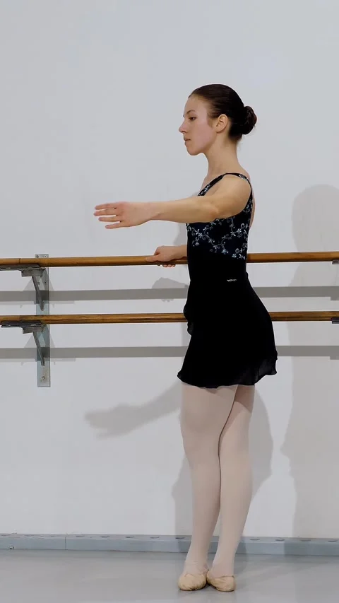 Ballet dancer in black leotard and white tights practicing posture at barre, Stock Footage 313798551