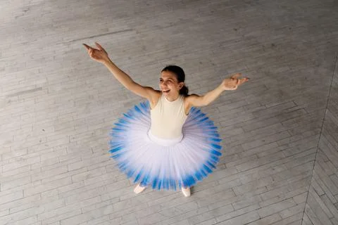 Ballet dancer in blue and white tutu performing a joyful pose on a light wooden Stock Photos