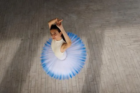 Ballet dancer in blue tutu performing graceful turn on wooden floor captured Stock Photos