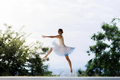 Ballet dancer leaping outdoors in a white and light-blue tutu on pointe against Stock Photos