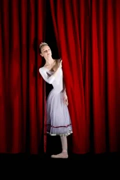 A ballet dancer peeking through a stage curtain, front view Stock Photos