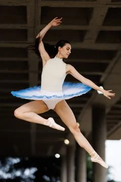 Ballet dancer performing high leap in white leotard and blue tutu on pointe Stock Photos