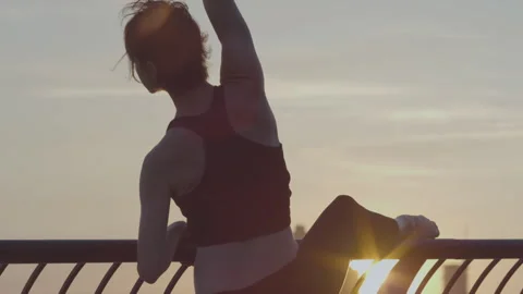 Ballet dancer performs elegant ballet workout by the riverside at sunset Stock Footage 312624087