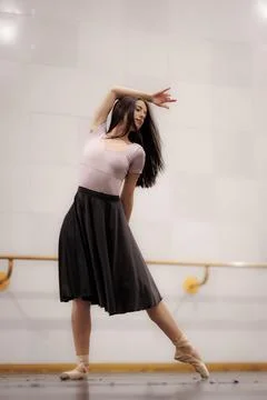 Ballet dancer practicing in a studio with wooden floors while performing a pose Stock Photos