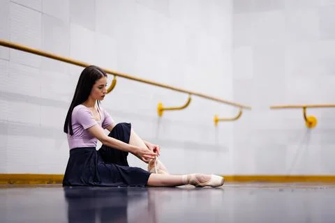 Ballet dancer ties pointe shoes in studio while preparing for practice in a Stock Photos