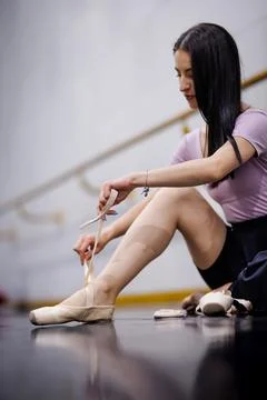 Ballet dancer ties ribbons on pointe shoes in a dance studio during a practice Stock Photos