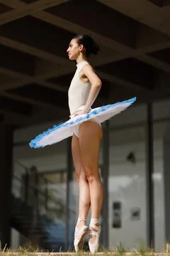 Ballet dancer in white tutu standing on pointe under modern architecture Stock Photos