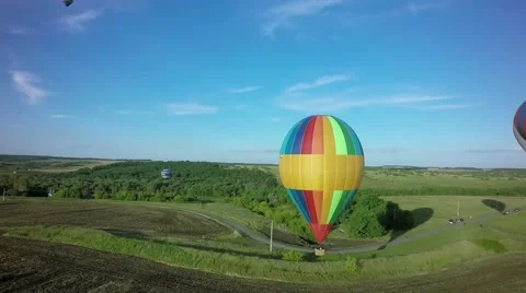 Balloons fly up in sky with passengers over green field 스톡 동영상 66007957