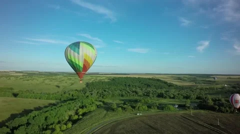 Balloons fly up in sky with passengers over green field Stock-Footage 66760837