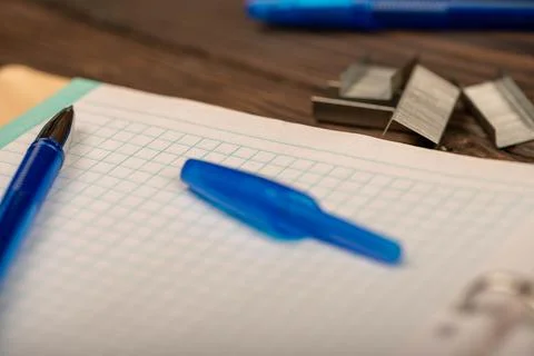 A ballpoint pen and a checkered notebook on a wooden table. Stock Photos