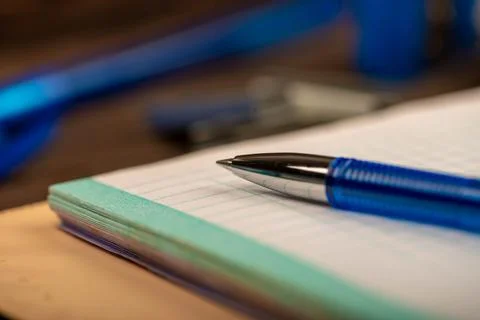 A ballpoint pen and a checkered notebook on a wooden table. Stock Photos