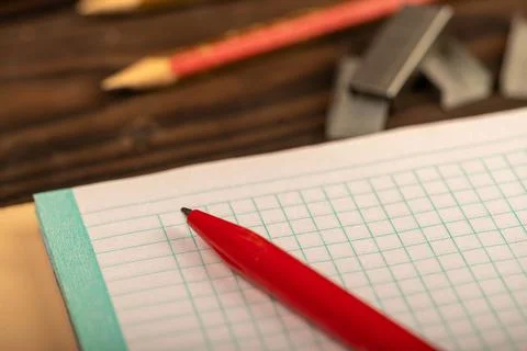A ballpoint pen and a checkered notebook on a wooden table. Stock Photos