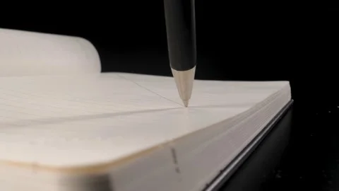 A ballpoint pen draws on a sheet of paper in a Notepad. Black background. Black  Stock Footage 144907251