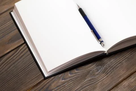 Ballpoint pen in open notebook on a dark brown wooden background. Blank pages Stock Photos