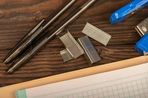 Ballpoint pen, stapler, and stapler staples a checkered notebook sheet on a w Stock Photos