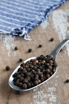 Balls of black pepper in a spoon on rustic background Stock Photos