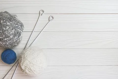 Balls of woolen thread and long metal needles on on light wooden boards backg Stock Photos