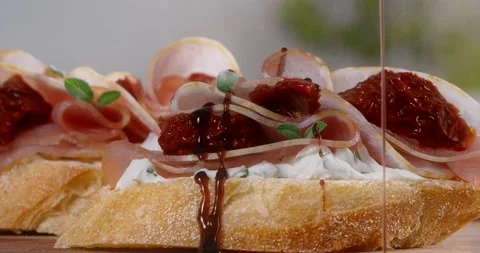 Balsamic is poured in slow motion to the bruschette with ham and dried tomatoes Stock Footage 168982114