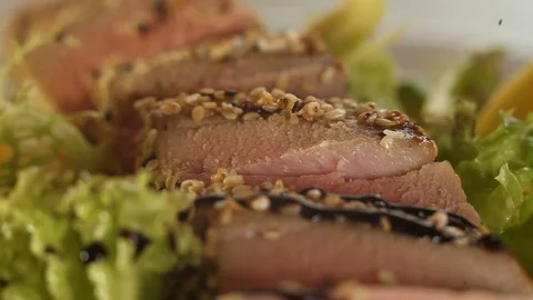 Balsamic sauce droplets fall on tuna pieces and green salad leaves on a plate Stock Footage 115486498