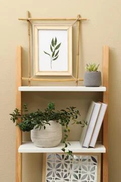 Bamboo frame and different decor elements on shelving unit near beige wall Stock Photos