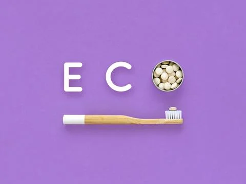Bamboo toothbrush and toothpaste in tablets. Word Eco on a violet background. Stock Photos