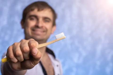 Bamboo toothbrush close-up on the background of a man out of focus. Stock Photos