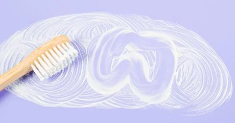 Bamboo toothbrush with smeared toothpaste and a painted tooth on a soft lilac 스톡 사진