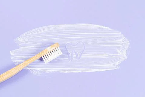Bamboo toothbrush with smeared toothpaste and a painted tooth on a soft lilac 스톡 사진