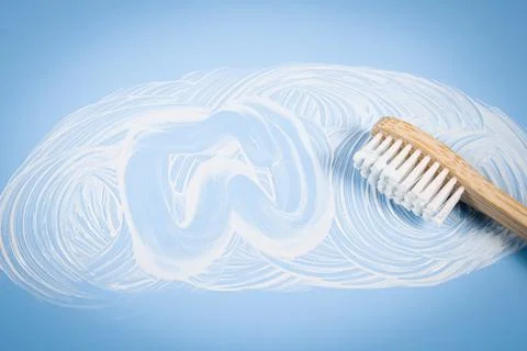 Bamboo toothbrush with smeared toothpaste and a painted tooth on a soft blue  스톡 사진
