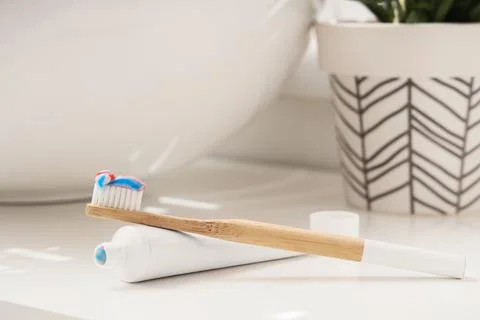 Bamboo toothbrush with striped toothpaste and white tube on bathroom countert Фото